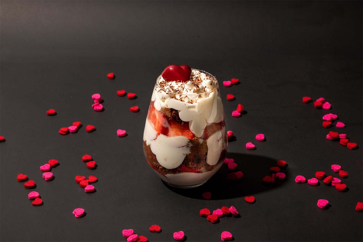 heart shaped confetti surrounding a parfait with a cherry on top on a black background