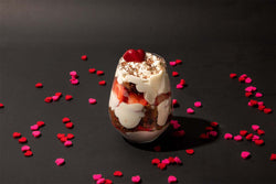 Image of heart shaped confetti surrounding a parfait with a cherry on top on a black background