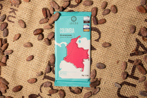 
            
                Load image into Gallery viewer, A teal chocolate bar wrapper, picturing an illustrated depiction of the country Colombia, sits on a burlap sack among scattered cocoa beans.
            
        
