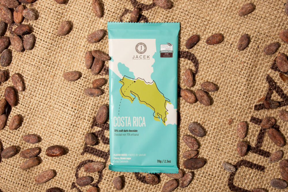 A teal chocolate bar wrapper, picturing an illustrated depiction of the country Costa Rica, sits on a burlap sack among scattered cocoa beans.