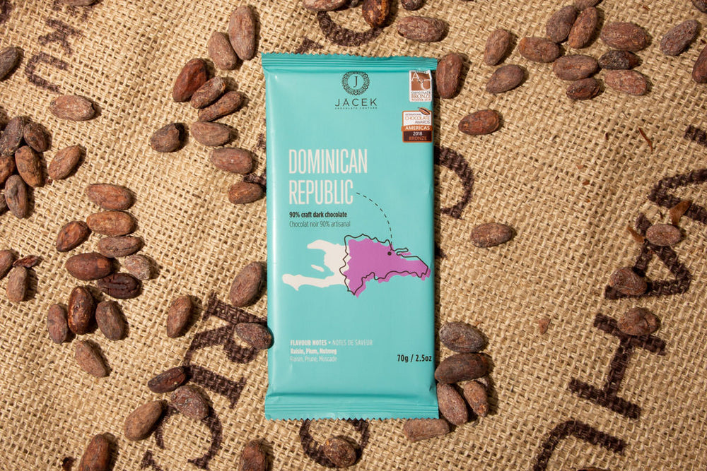 
            
                Load image into Gallery viewer, A teal chocolate bar wrapper, picturing an illustrated depiction of the country Dominican Republic, sits on a burlap sack among scattered cocoa beans.
            
        
