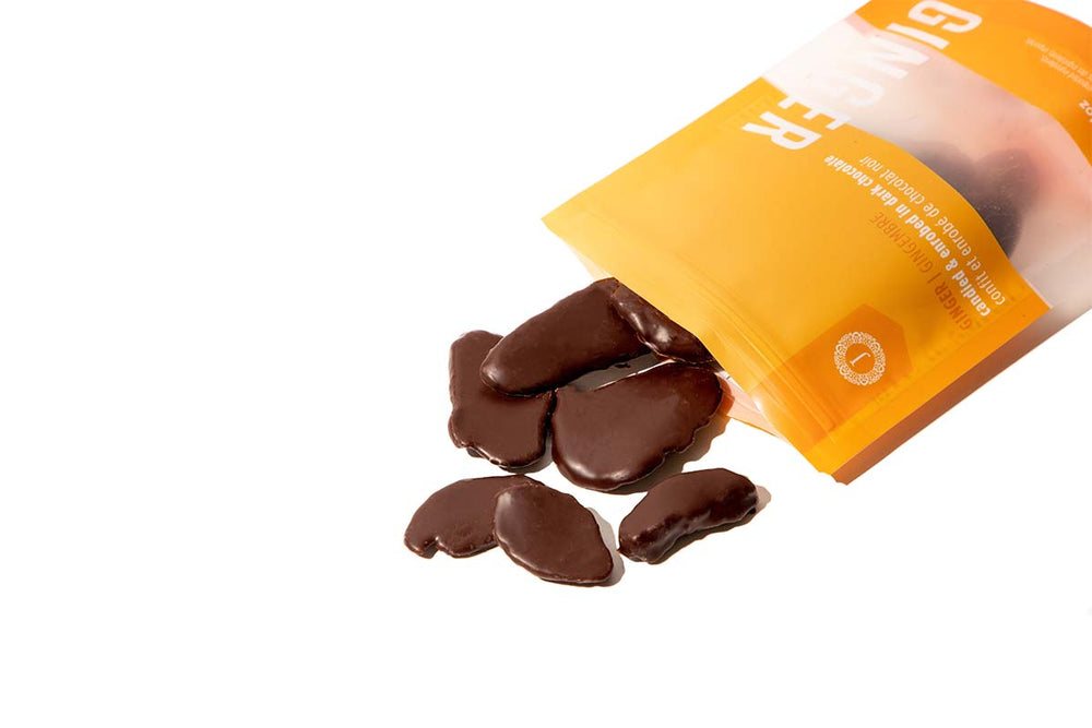 
            
                Load image into Gallery viewer, The yellow Candied Ginger pouch lays on its side, with pieces of candied ginger spilling out.
            
        